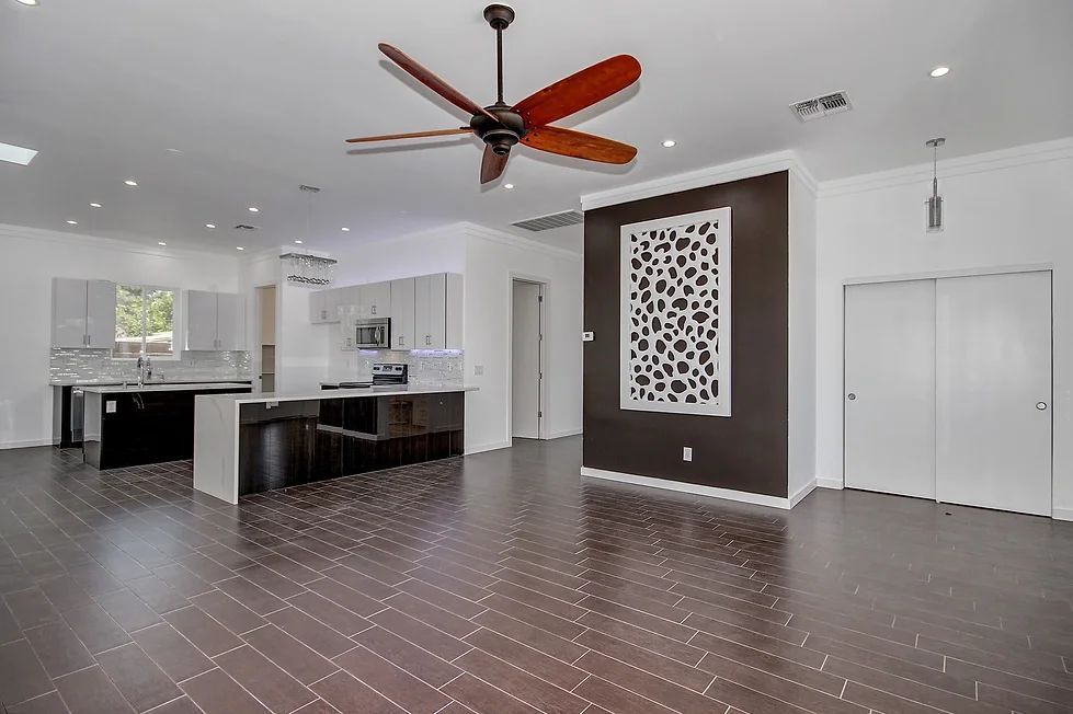 A living room with a ceiling fan and a kitchen in the background.