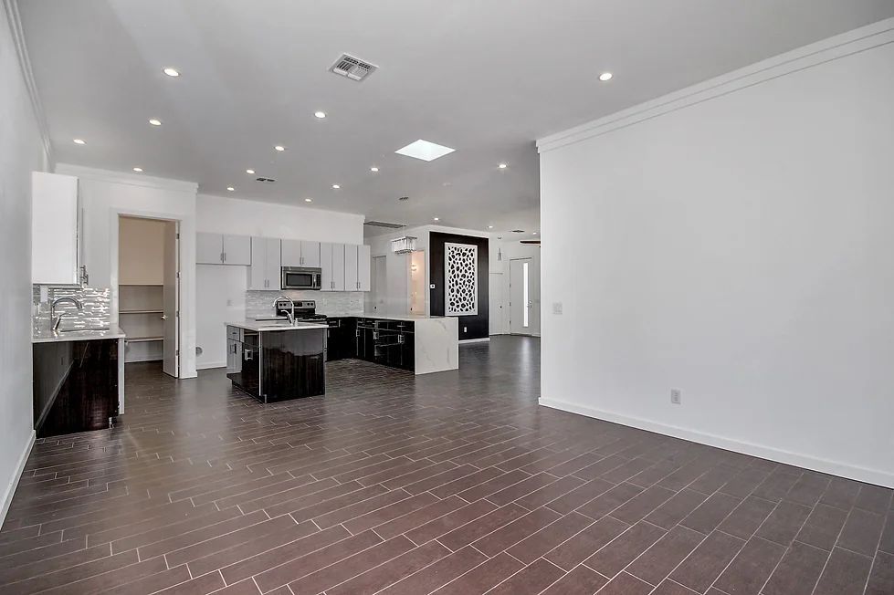 A large empty room with a wooden floor and a kitchen in the background.