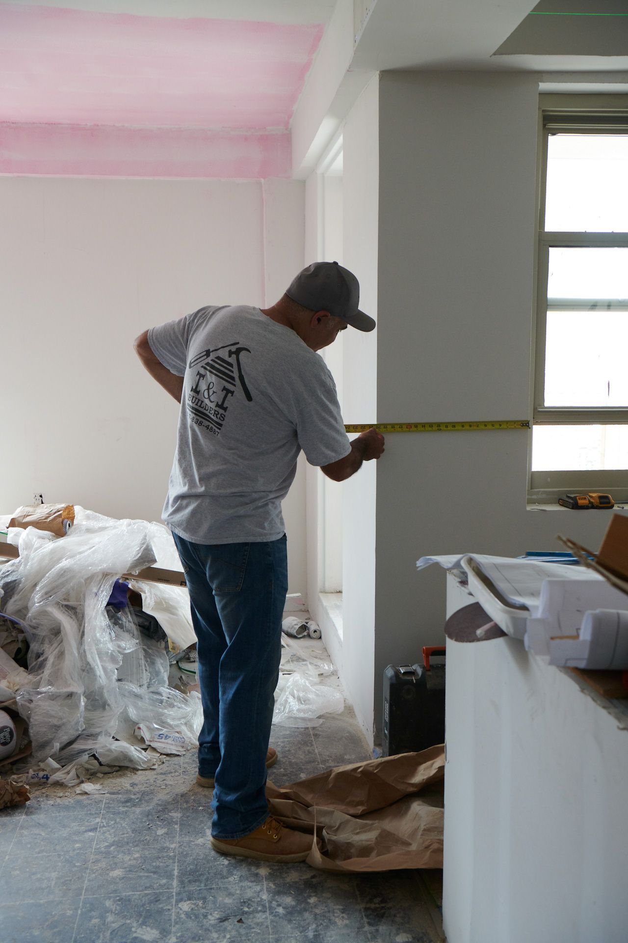 A man is measuring a wall with a tape measure in a room.