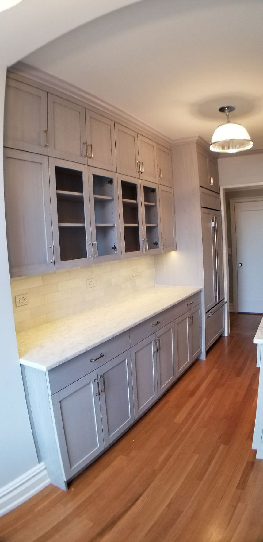 A kitchen with gray cabinets, white counter tops, and hardwood floors.
