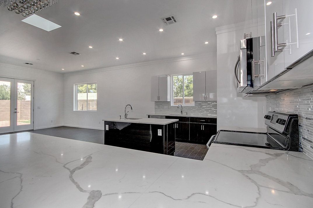 A kitchen with white cabinets, black counter tops, a stove and a sink.