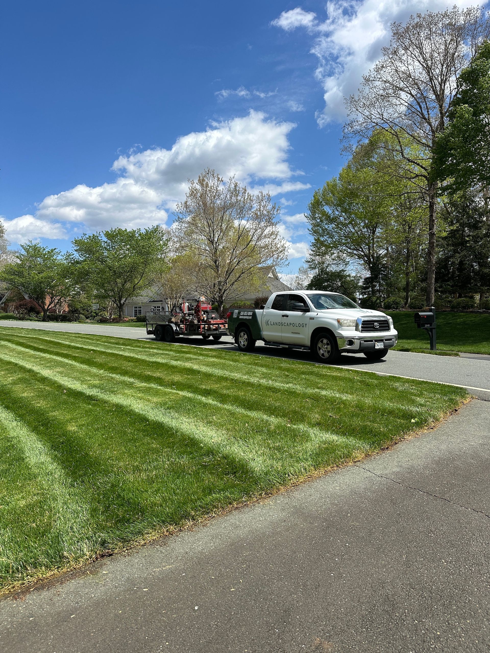 A white truck is parked on the side of a road next to a lush green field.