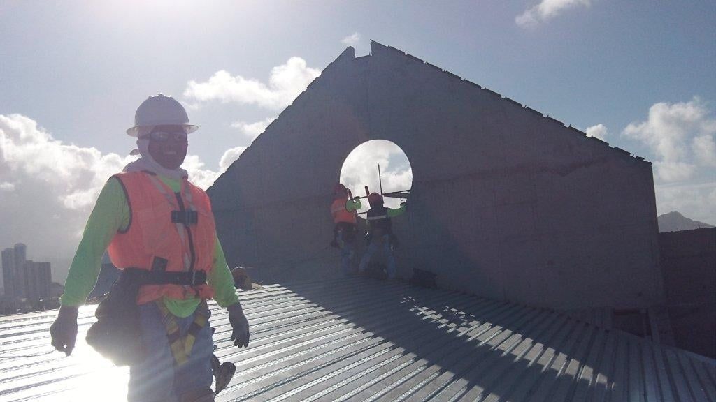 A construction worker is standing on top of a metal roof.