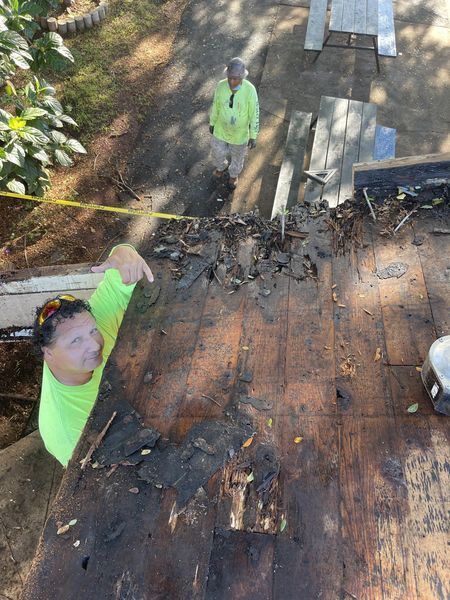 A man in a green shirt is standing on top of a wooden roof.