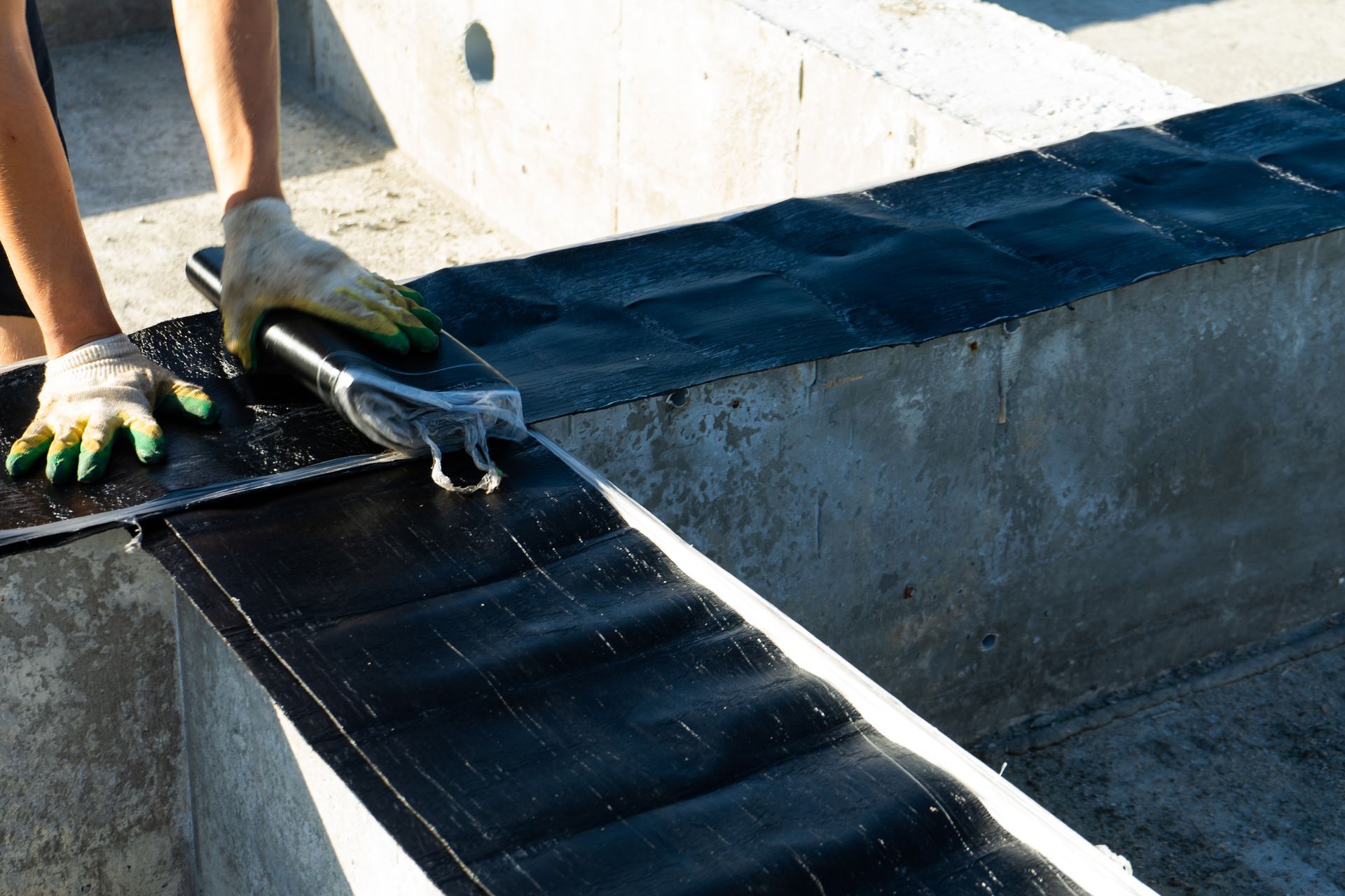 Person smoothing sealant on black waterproof membrane on a concrete structure.