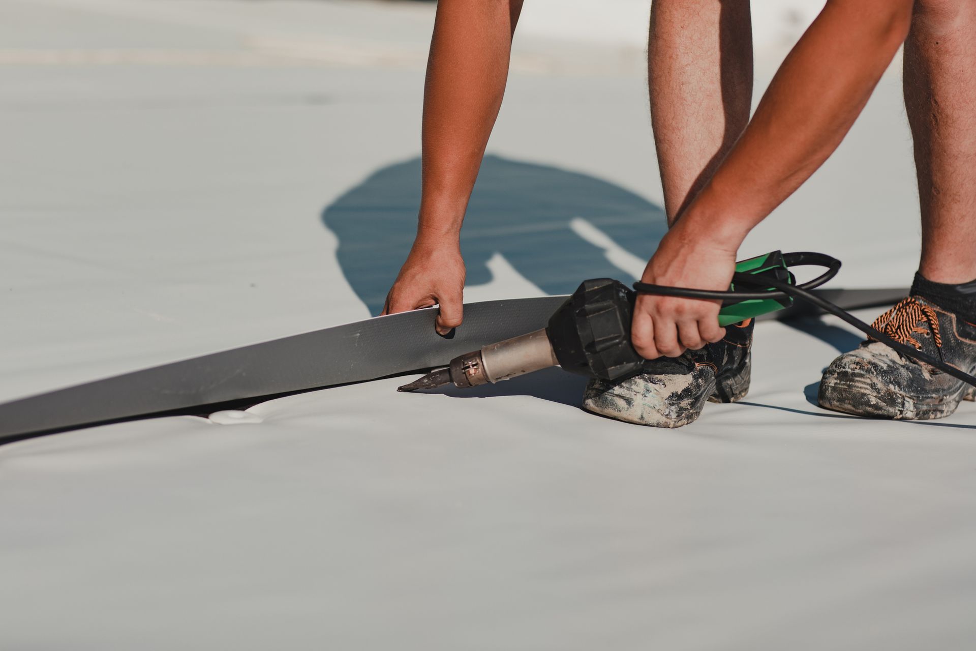 Person using a heat gun to seal a dark strip to a white surface on a rooftop.