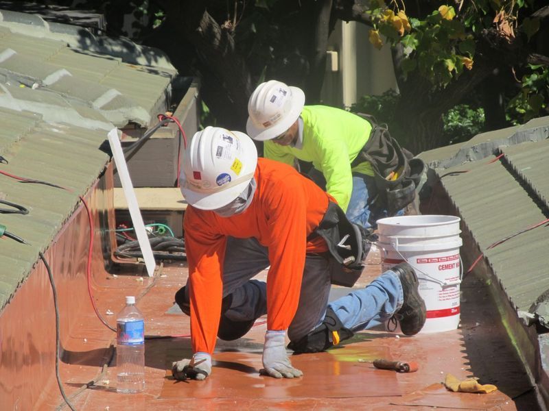 Two men wearing hard hats are working on a roof