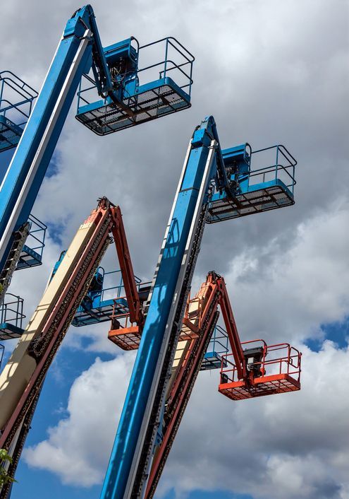 Blue and orange boom lifts reaching towards a cloudy sky.