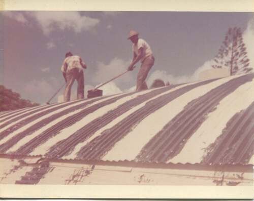 Two men are painting a roof with a broom.