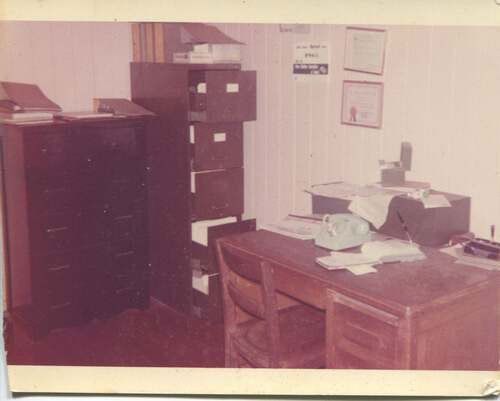 An old photo of an office with a desk and chairs