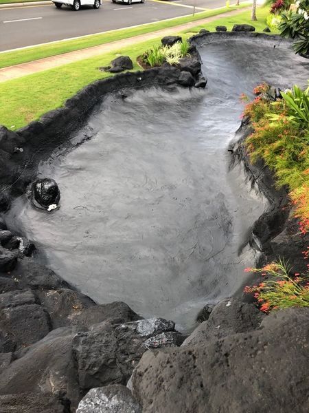 A small pond surrounded by rocks and grass next to a road.