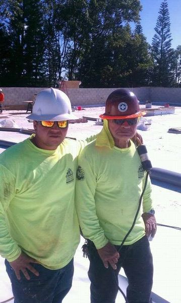 Two construction workers wearing hard hats and neon green shirts are posing for a picture.