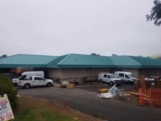 A building with a green roof and white vans parked in front of it.