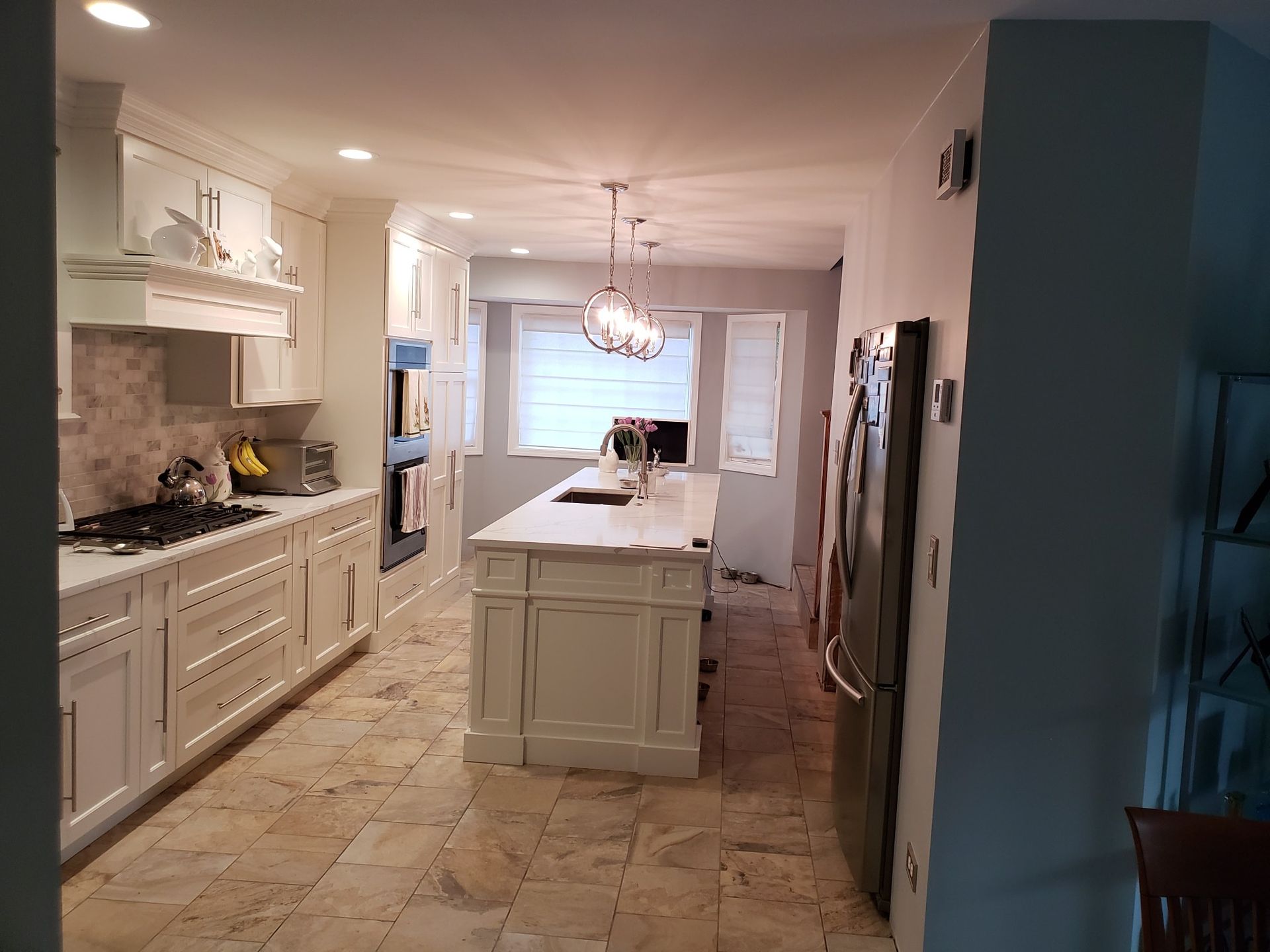 White kitchen with island, cabinets, appliances, and tile floor.