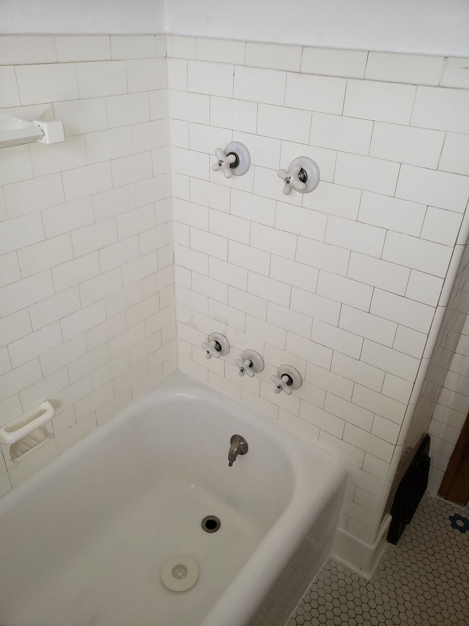 White tiled bathtub with exposed plumbing fixtures.