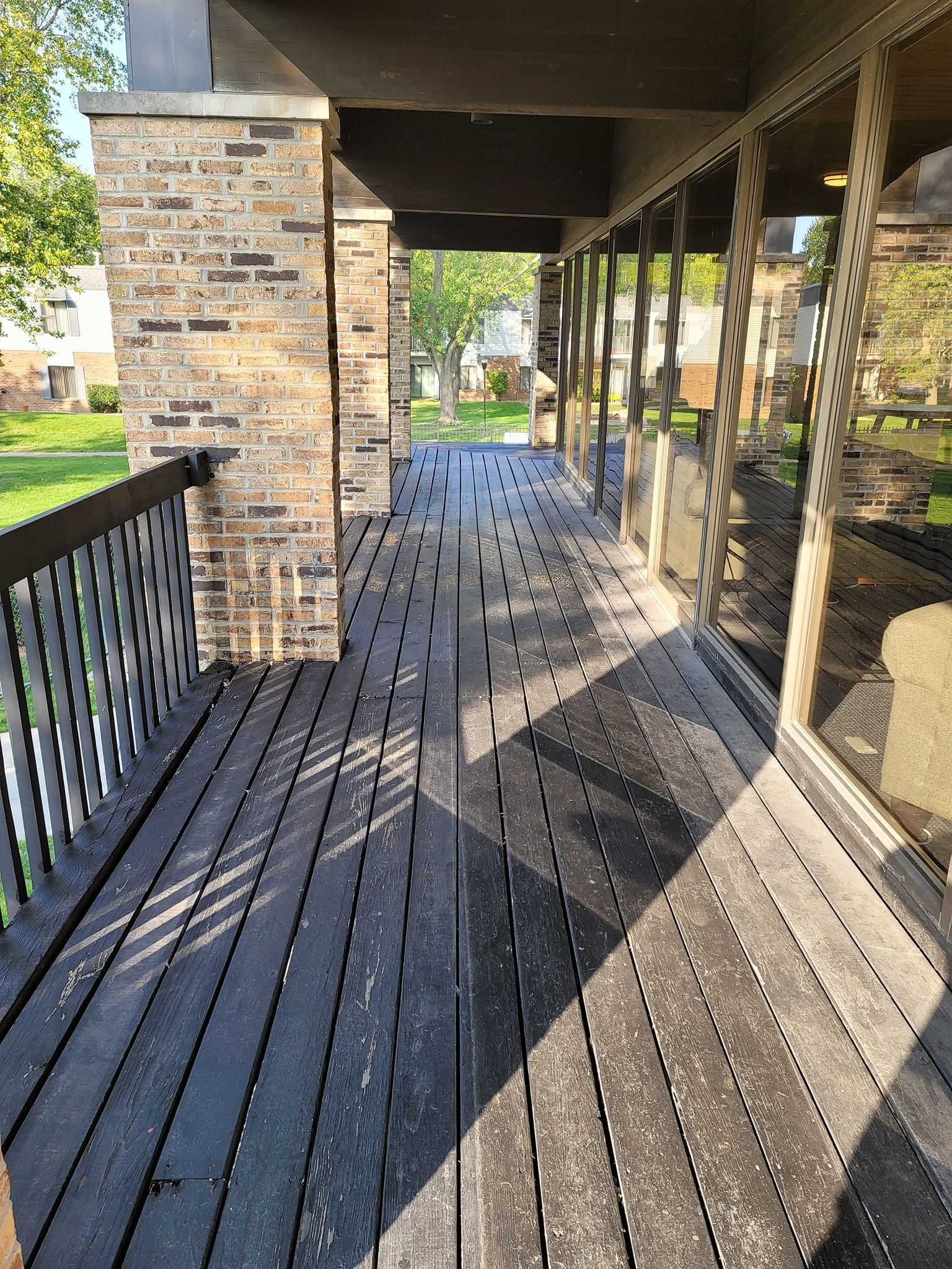 Covered wooden deck with black railings and brick pillars. Glass windows line the right side.