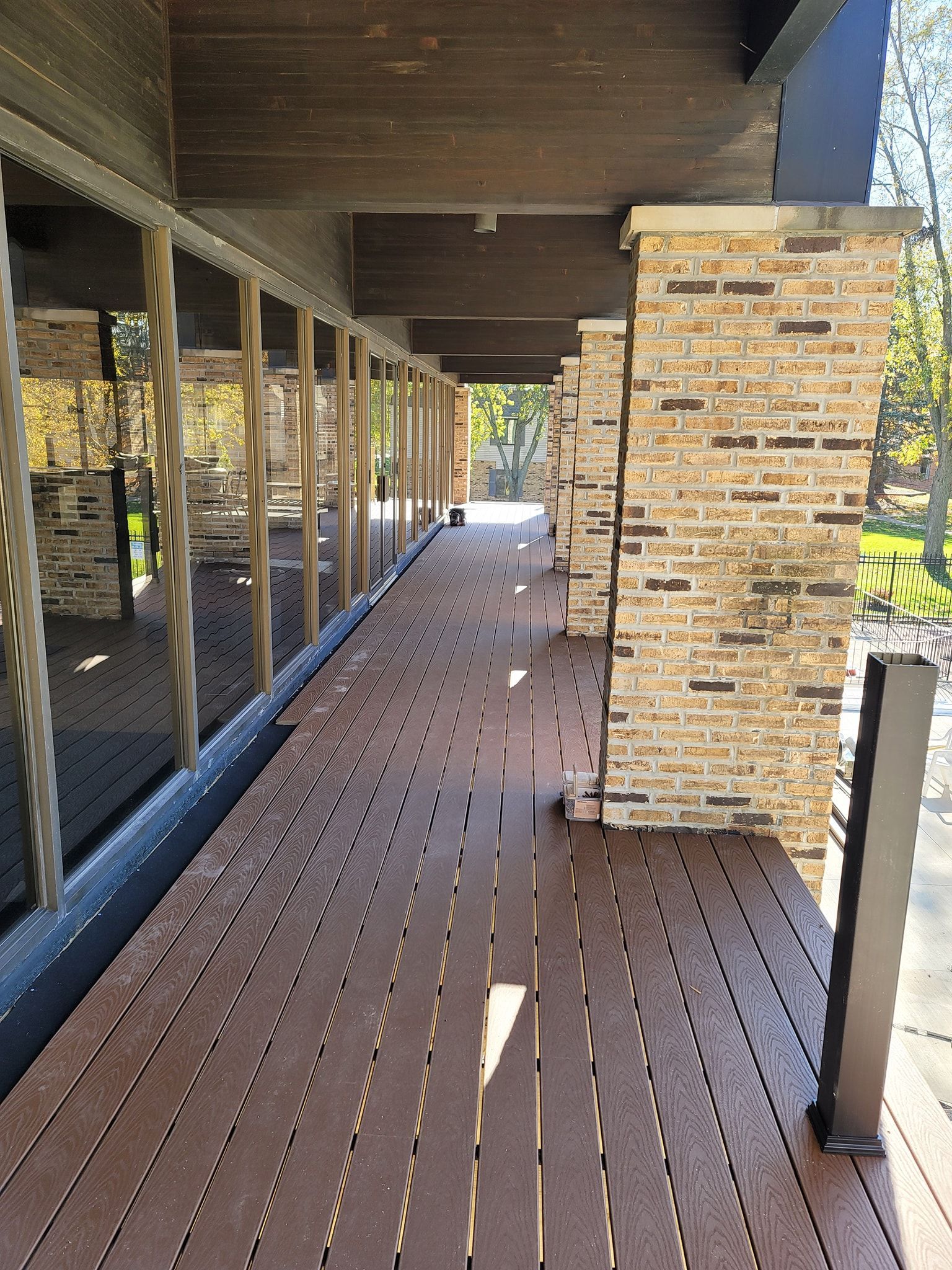 Long wooden deck with brown planks and brick pillars, leading to an open area with sunlight.