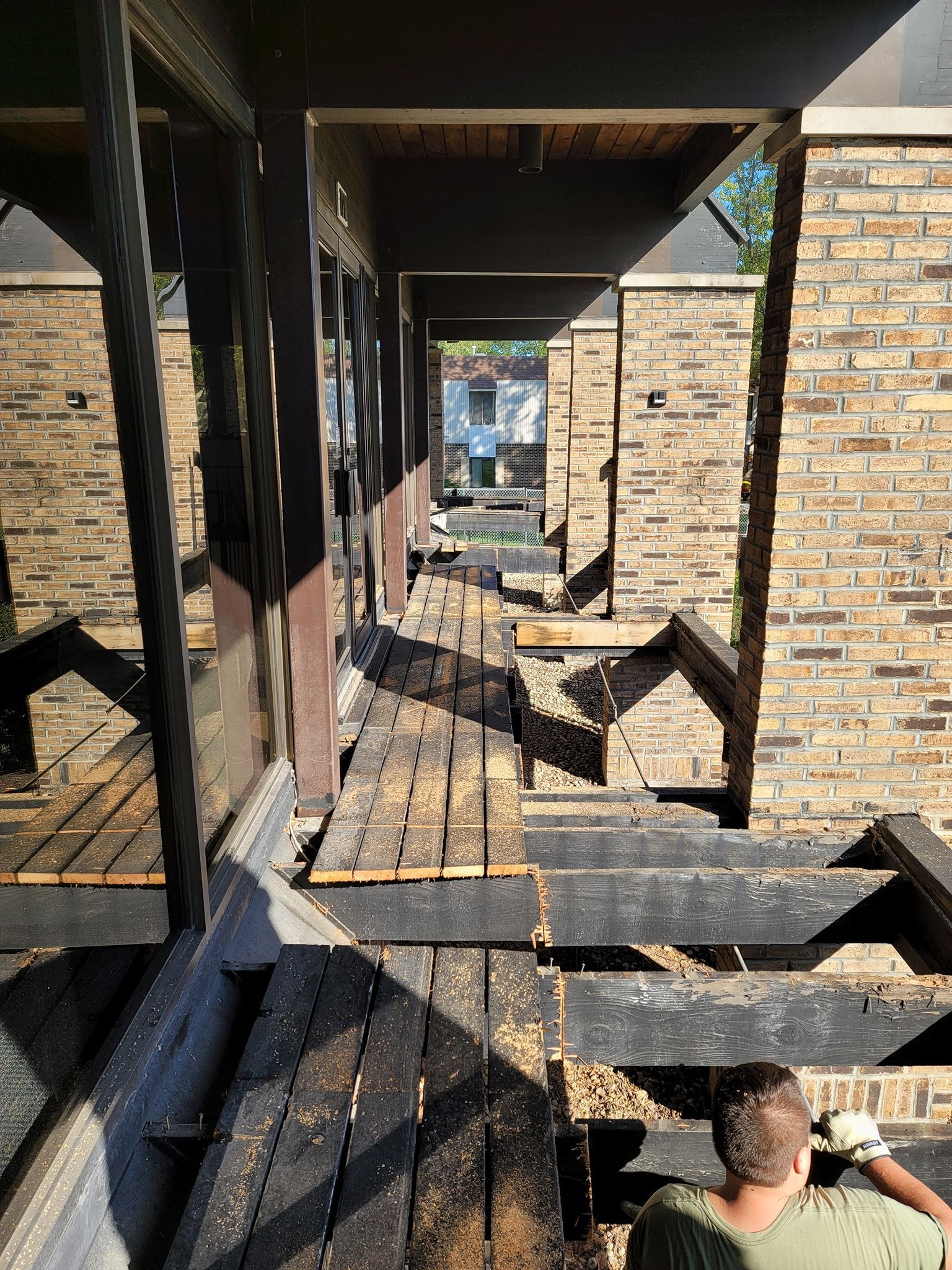 Damaged wooden walkway with brick pillars, debris, and a person's back, outdoor setting.