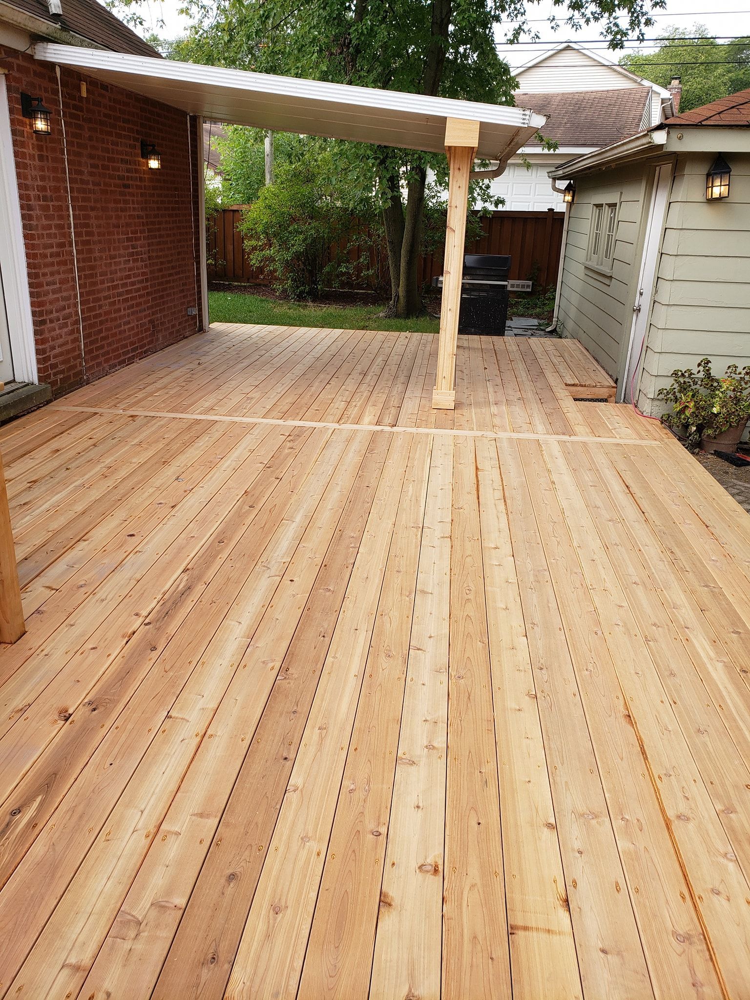 Wooden deck with a pergola attached to a brick wall. A shed is to the right.