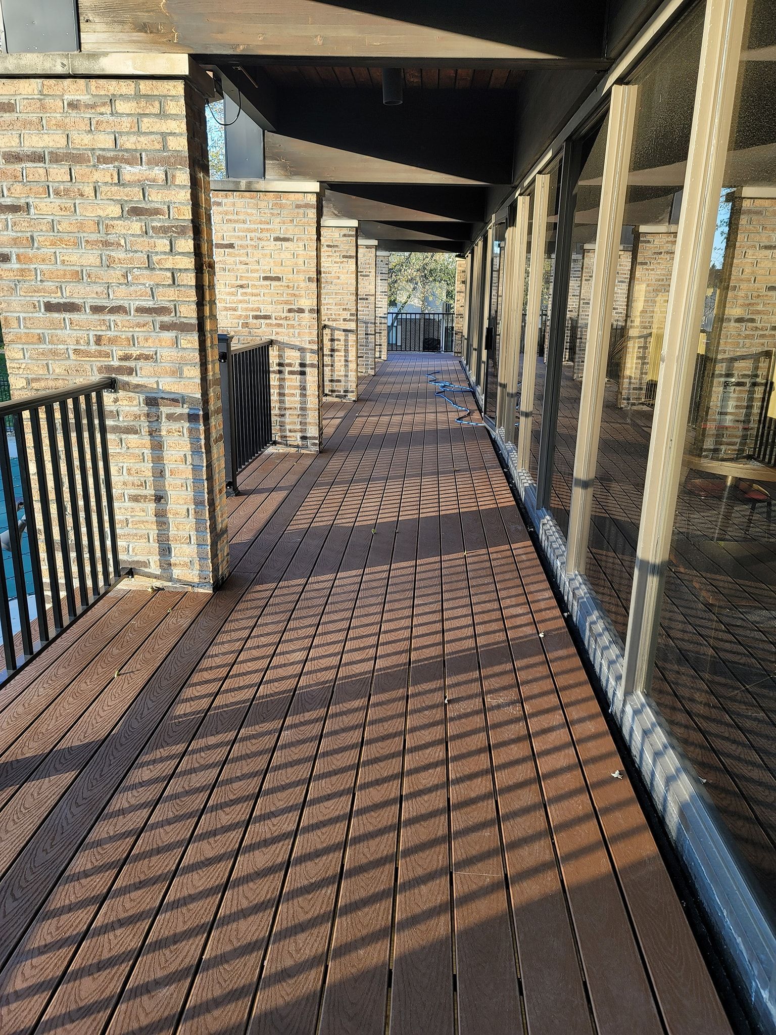 Long, brick-paved patio with a brick wall on one side and windows on the other, sunny.
