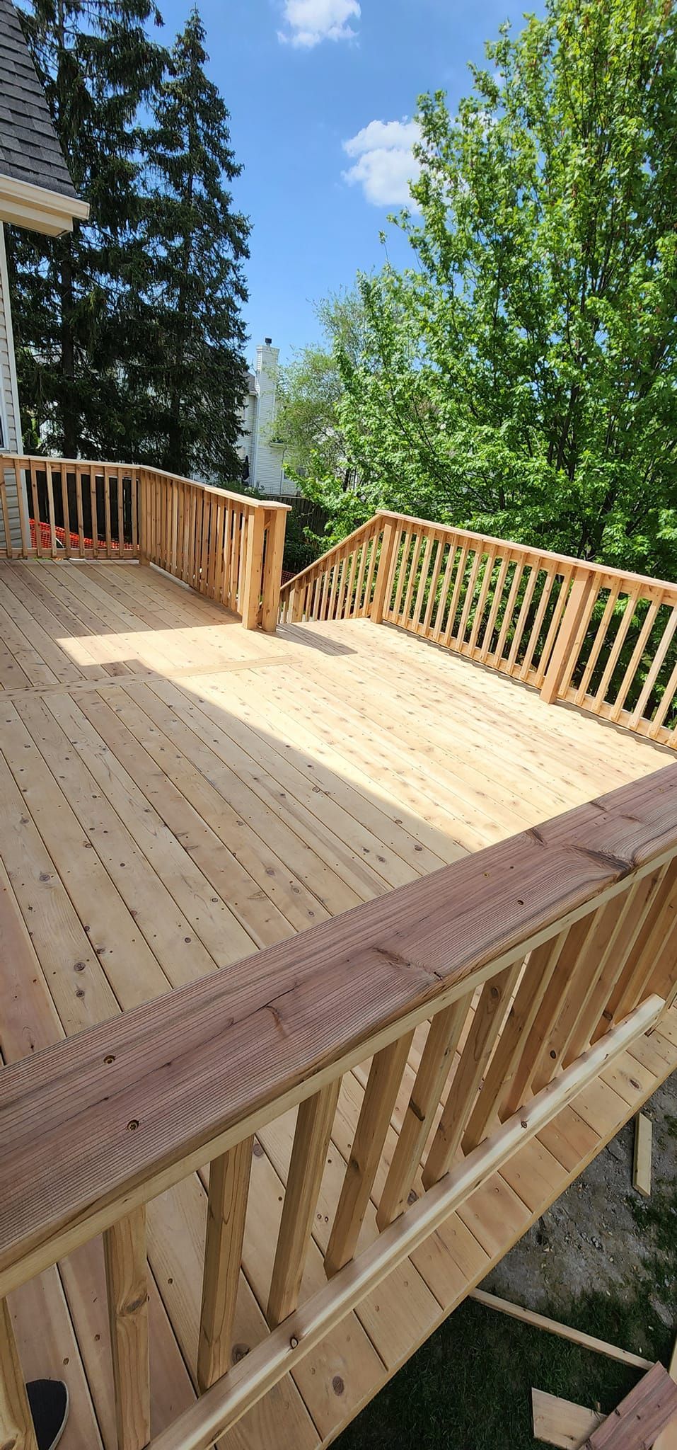 A wooden deck with railings, surrounded by trees and a blue sky.