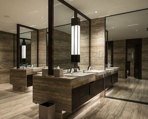 Public restroom with stone walls, sinks, mirrors, and a tall central light fixture.
