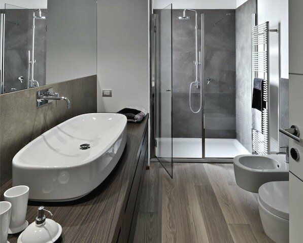 Modern bathroom with a vessel sink, glass shower, toilet, and wooden floor.