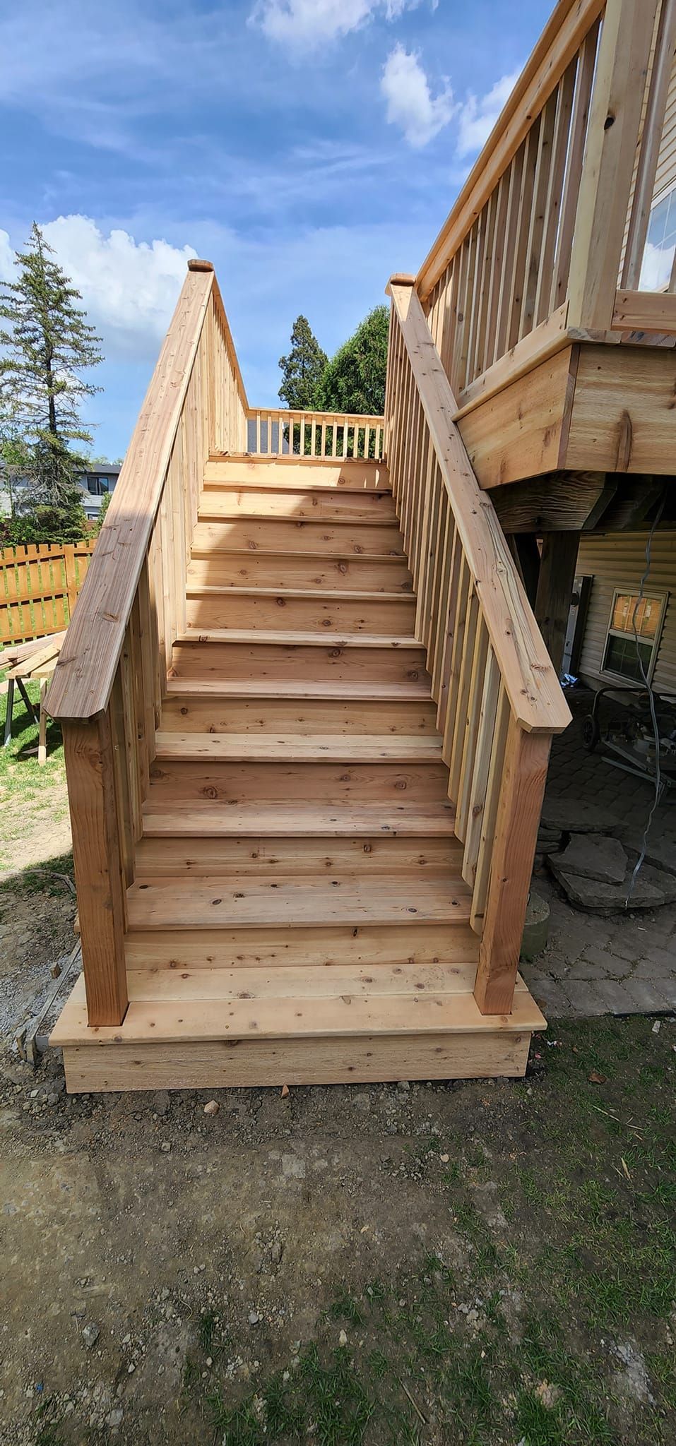 Wooden staircase leading up to a deck, set against a blue sky with some trees.