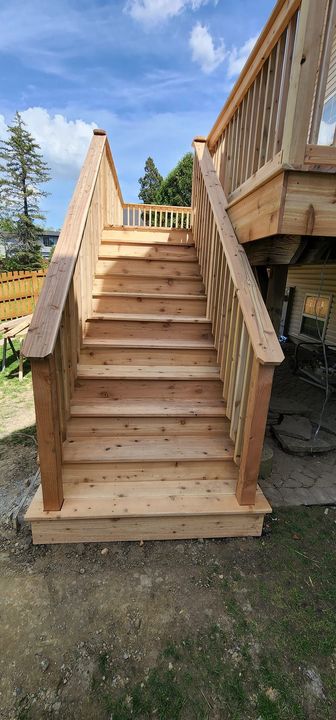 Wooden outdoor staircase leading up to a deck, set against a blue sky with some greenery.