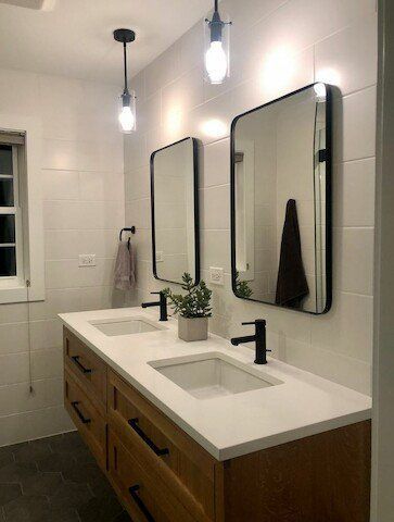Modern bathroom with a wooden vanity, two mirrors, and pendant lights.