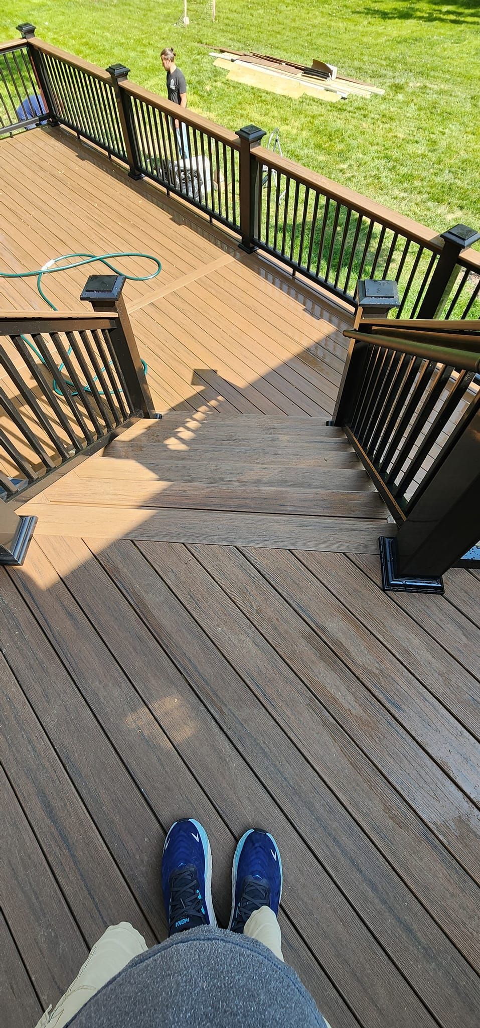 Person standing on a wooden deck with stairs leading down. Grass surrounds the deck. Blue shoes.