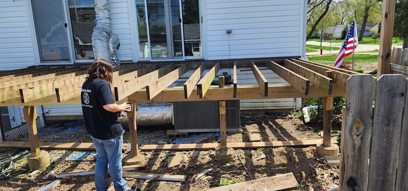 A person rebuilding a deck next to a white house with an American flag.