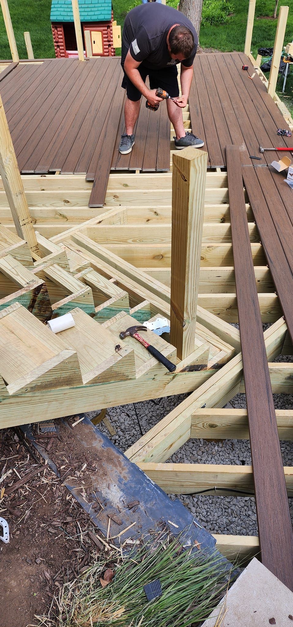 A person is working on a wooden structure, possibly a deck or roof, with tools in hand.