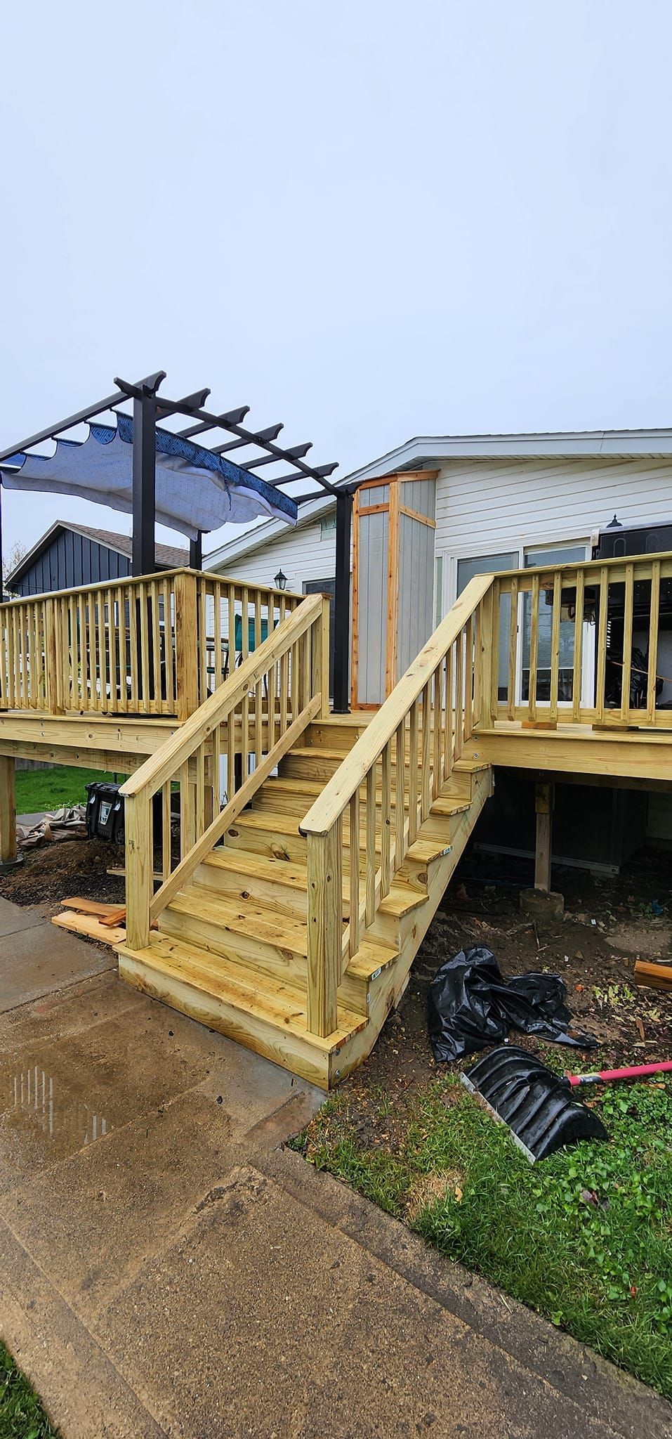 New wooden deck with stairs and pergola. Exterior setting, overcast sky.