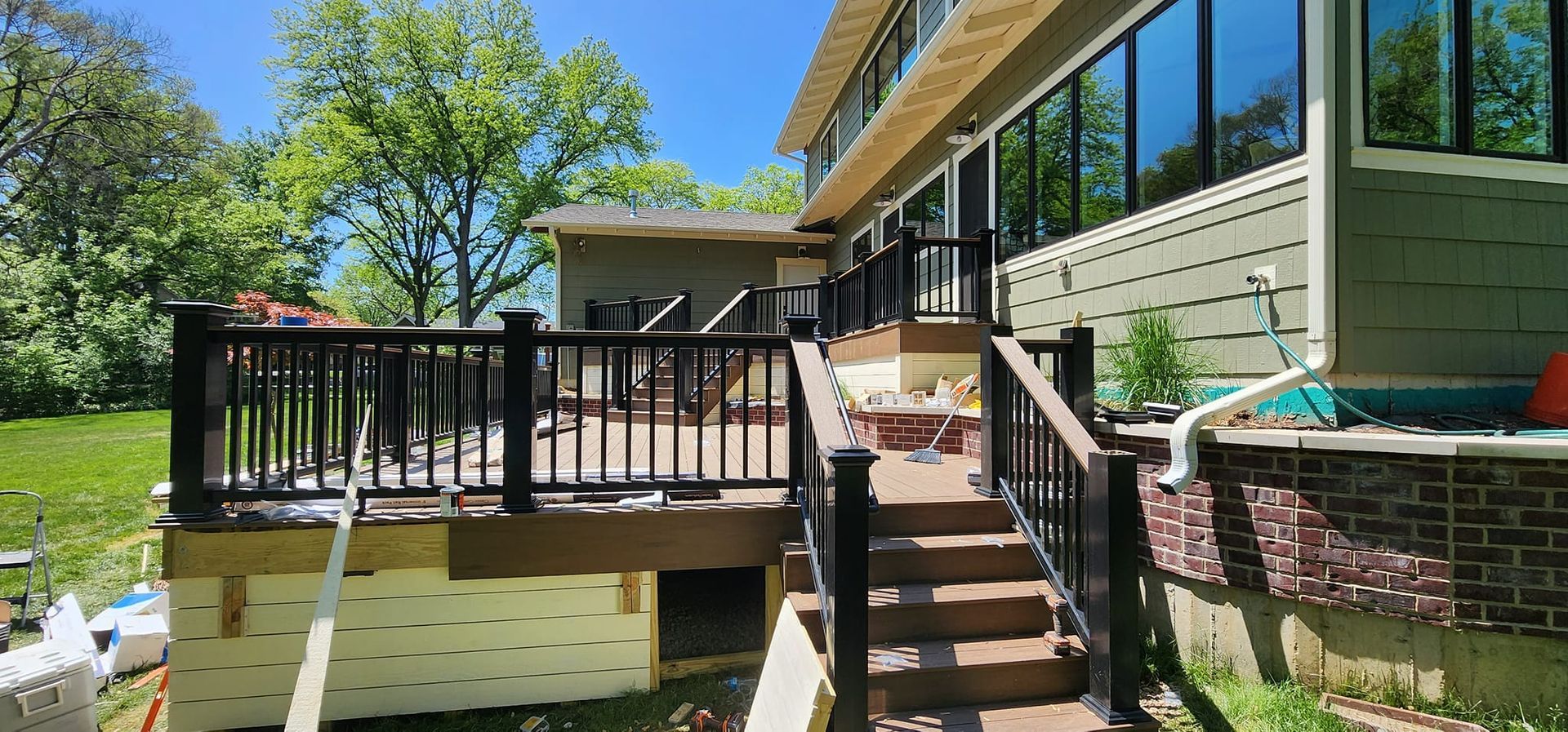 Exterior view of a house with a deck and stairs. Black railings, green siding, blue sky.