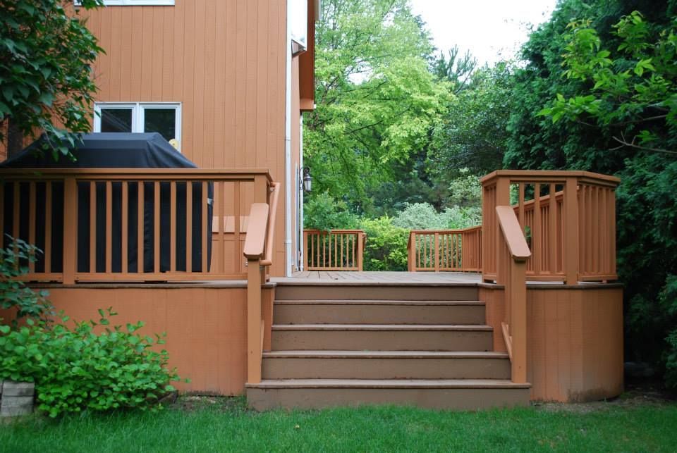 Wooden deck with steps leading into a yard with greenery. Brown painted deck and railing.