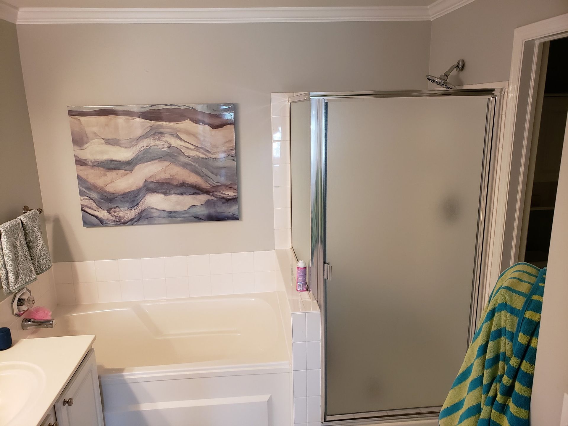 Bathroom with a tub and frosted glass shower door, light gray walls, and a watercolor painting.