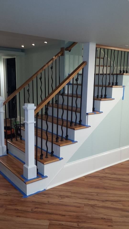 Wooden staircase with black metal balusters and white risers, being painted in a home.