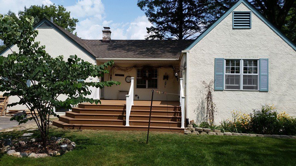 Cottage-style house with steps and porch, light stucco exterior, blue shutters. Green grass and small tree in front.