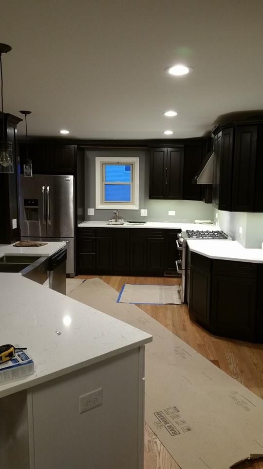 Dark kitchen with white countertops, stainless steel appliances, and wood flooring.