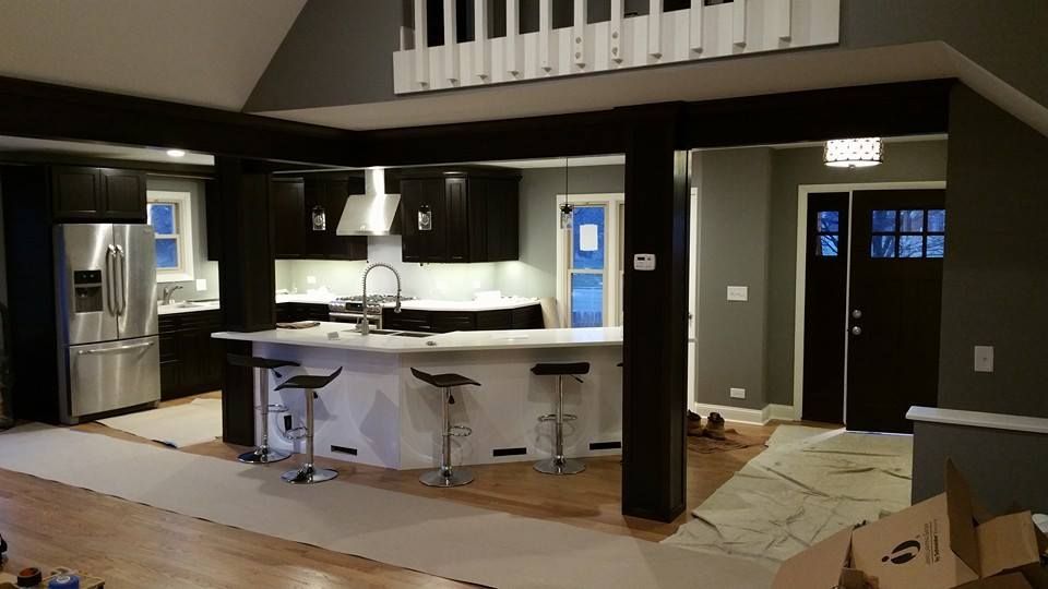 Modern kitchen with dark cabinetry, white countertops, and wood flooring; connected to a living area.