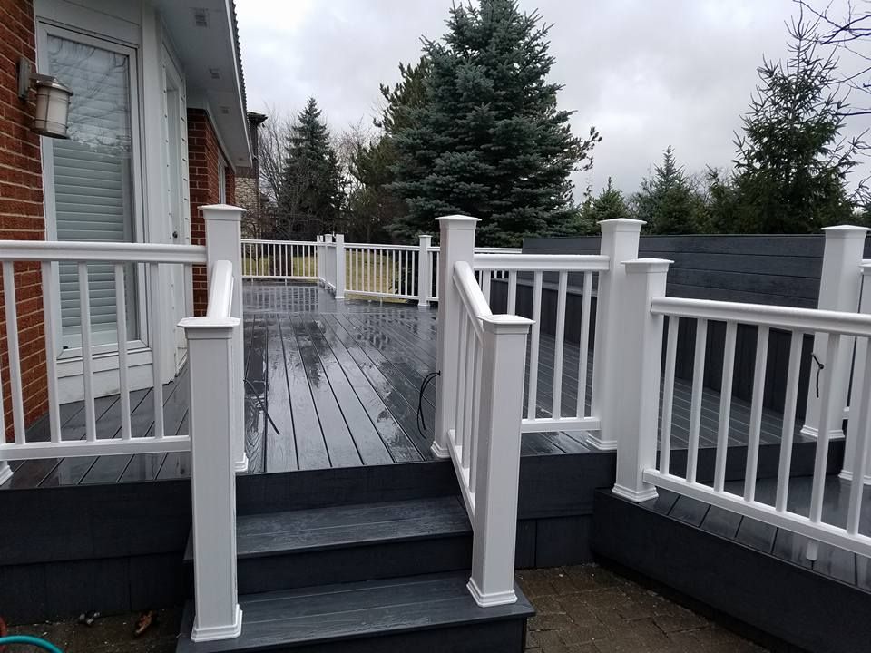 Gray composite deck with white railings and steps, brick building visible.