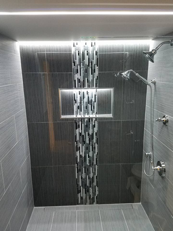 Gray tiled shower with a decorative mosaic strip and two showerheads.