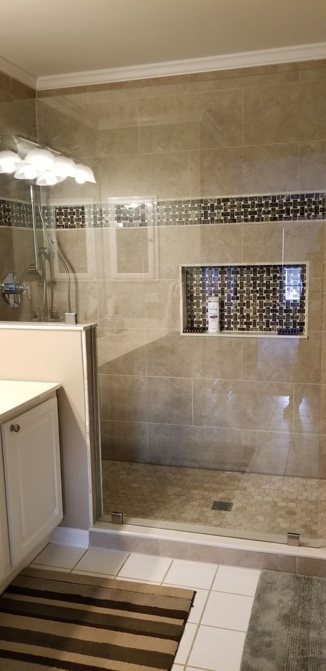 A bathroom with beige tile walls, a glass shower door, and a white vanity with a striped rug on the floor.
