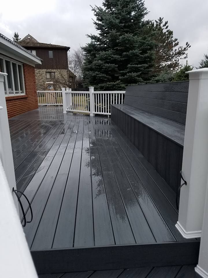 Gray composite deck with a built-in bench and white railing. Wet surface, overcast sky.