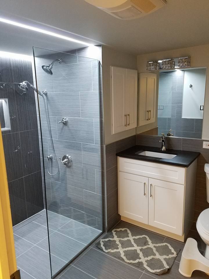 Modern bathroom with gray tiled shower and vanity, white cabinets, and a patterned rug.