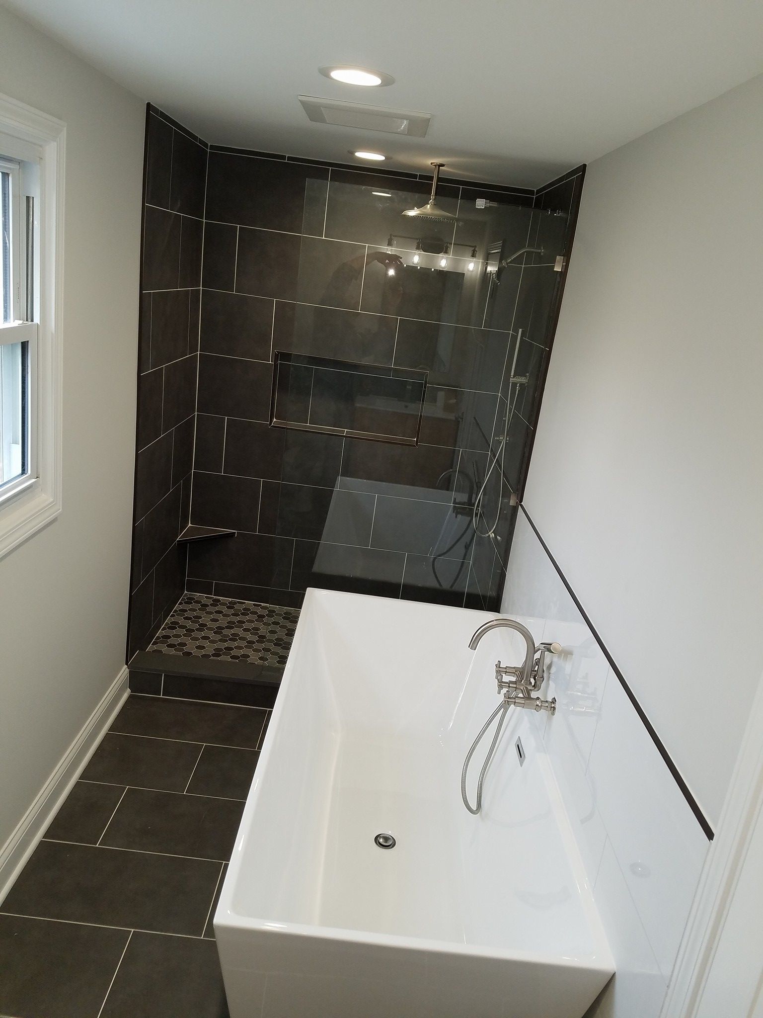 Modern bathroom with a dark tiled shower, soaking tub, and window.