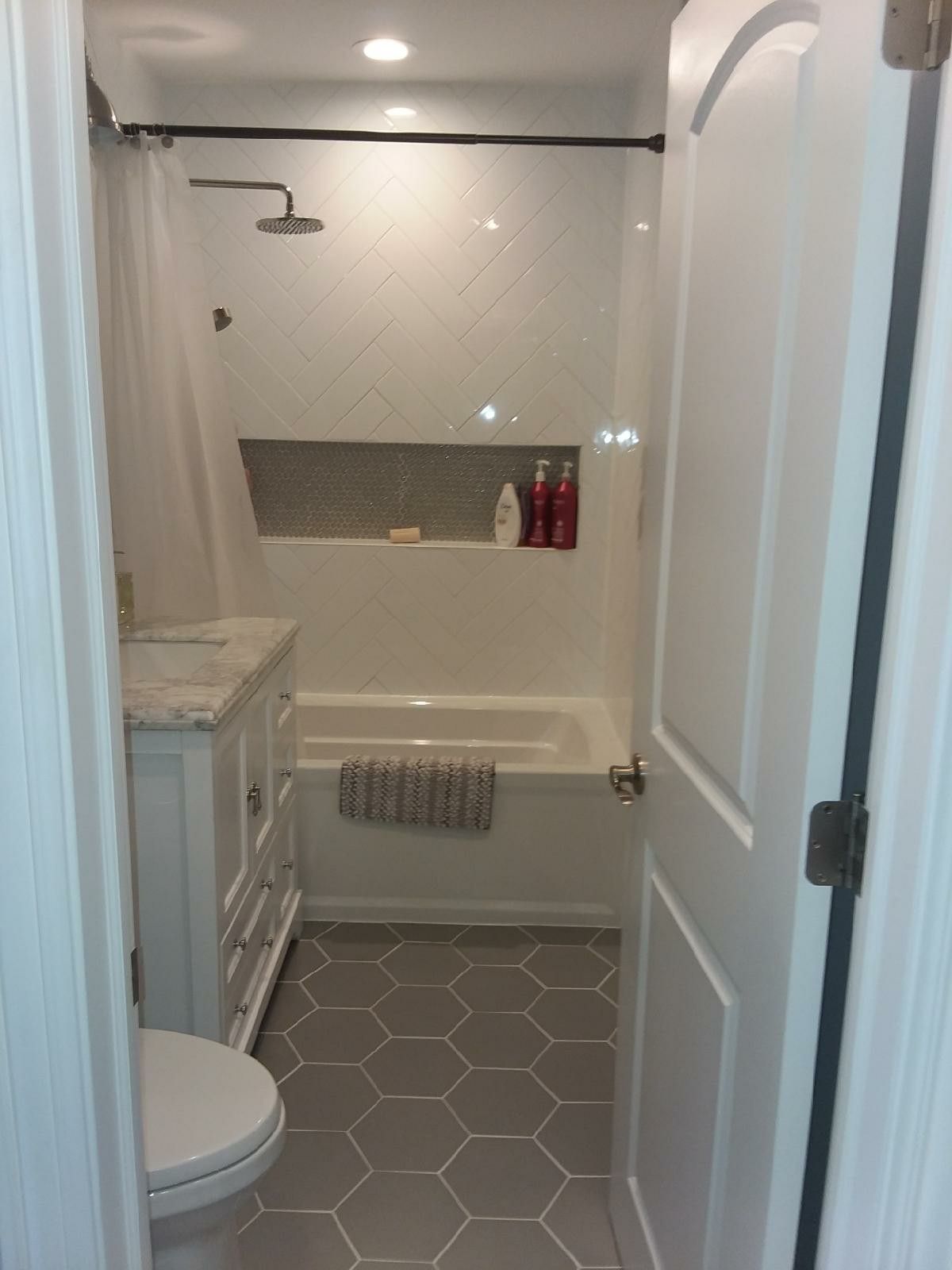 Small white bathroom with hexagon tile floor, shower, vanity, and toilet.