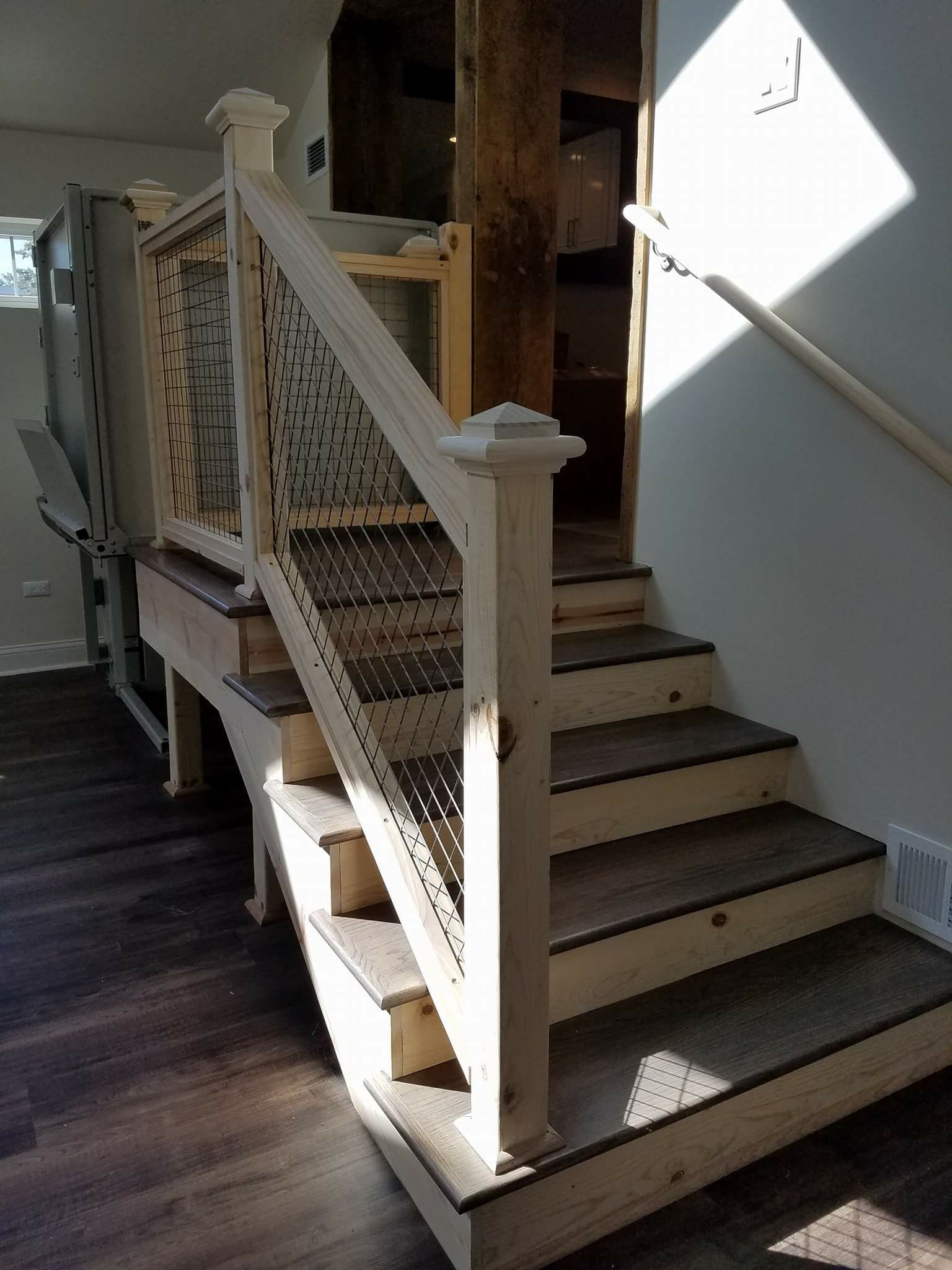 Wooden staircase with ornate railing and metal mesh treads, leading up to a doorway.