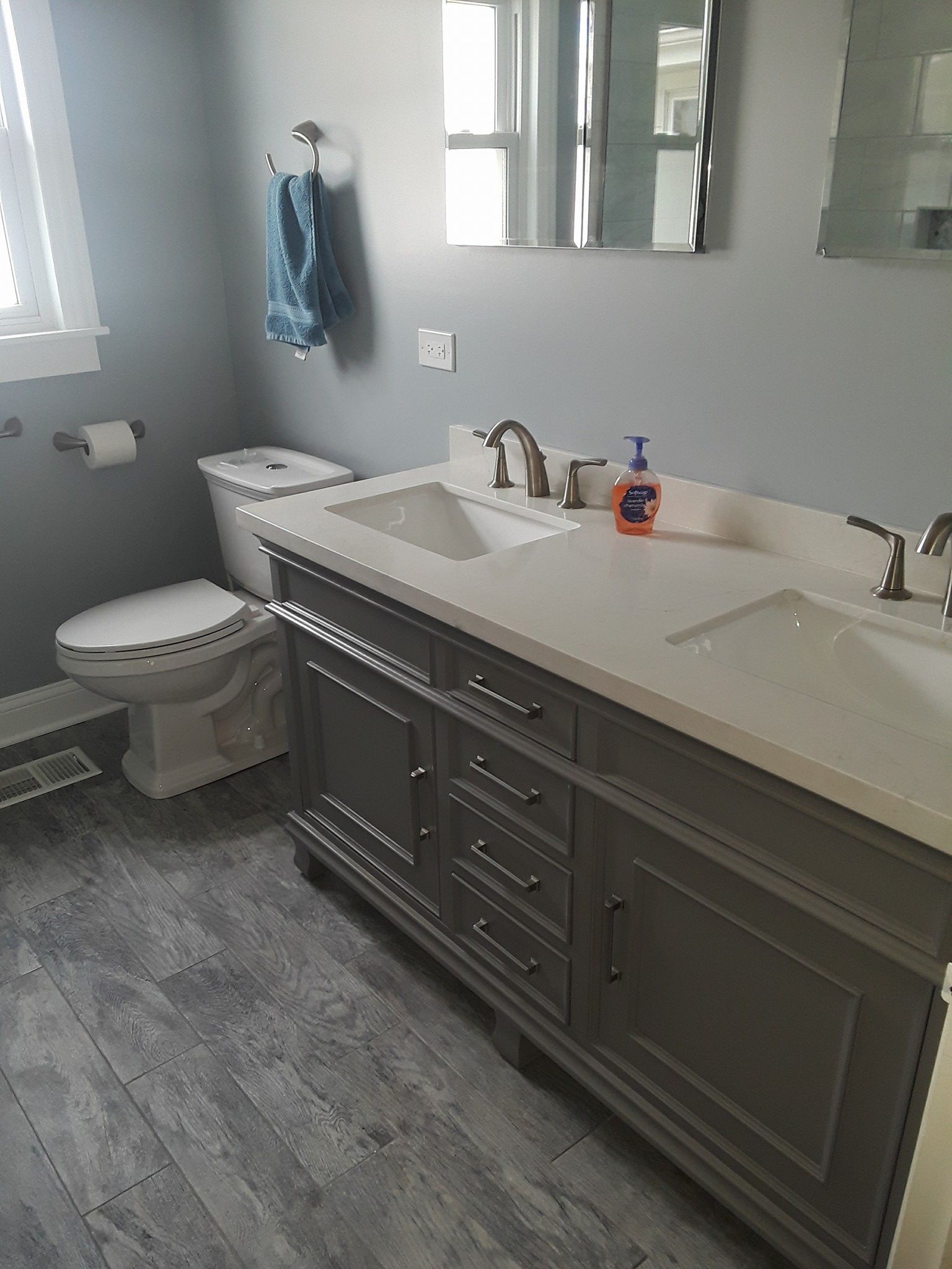 Bathroom with a gray vanity, white countertops, and toilet. Gray and white color scheme.